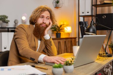 Sıkıcı, uykucu, sakallı iş adamı dizüstü bilgisayarda çalışıyor, ofis masasına yaslanıyor. Yorgun, Kafkasyalı, kızıl, serbest çalışan, işkolik bir adam. İstihdam, meslek, işsiz.