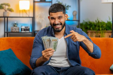 Başarılı Hintli adam elinde dolar banknotları tutan bir hayranı sınıftaki kanepede oturuyor. Mutlu İspanyol adam çevrimiçi kumarhane oyunu kazanarak tatil planlama bütçesini hesaplıyor.