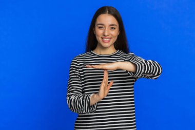 Mutlu gülümseyen genç kadın mola hareketi yapıyor, sınır veya dur işareti yok baskı yok, daha fazla zamana ihtiyacım var. Güzel, esmer, yetişkin bir kız, mavi arka planda izole olmak isteyen çalışmaktan sıkılmış.