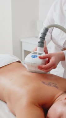 Kozmetikçi doktor sırtında LPG elektrikli süpürge masaj prosedürü uygular. Kaplıca salonundaki düzeltme figürleri. Vücut şekillerini geliştiriyor. Kilo kaybı, lenf drenajı. Dikey