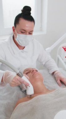 Güzellik uzmanı kadın RF kaldırma prosedürü yapıyor. Yüz ve göğüs, kolajen maskesi. Kozmetik uzmanı vakum masaj terapisi için elektrikli ekipman kullanıyor. Cilt bakımı, güzellik tedavisi. Dikey