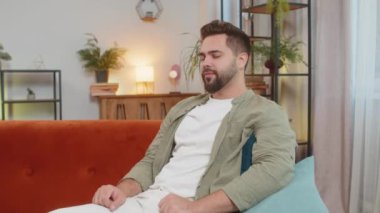 Kameraya gülümseyen, el sallayan, el sallayan, evdeki oturma odasındaki kanepede otururken selamlaşan mutlu beyaz adam. Mutlu sakallı adam evde video kaydediyor..