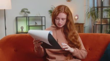 Finansal grafik belgeleriyle çalışan genç kadın muhasebeci, çizelgeler için vergileri hesaplıyor ve kanepedeki ev gelirlerinin grafiklerini çıkarıyor. Kanepede oturan kızıl saçlı, harcama bütçeli yetişkin kız..