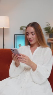 Aman Tanrım. Vay canına. Akıllı telefon daktilosu kullanan mutlu, heyecanlı beyaz kadın harika bir galibiyet elde etti. İyi haber zaferi kutluyor. Cep telefonlu bir kız, evinde, kanepede oturuyor. Dikey