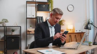 Çevrimiçi akıllı telefon uygulaması kullanan kendine güvenen genç bir işadamı, işaret ederek iyi niyet gösteriyor, uzaktan kumandalı bir iş. Kameraya bakan serbest çalışan yakışıklı bir adam. Reklamcılık