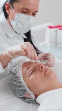 Kozmetik uzmanı özel asit serumu uyguluyor. Tıbbi kremi nemlendiriyor, güzel beyaz bir kadının yüzünü ovuyor. Bir güzellik salonunda yüz bakımı yaşlanmayı önleyen kozmetik tedavi prosedürü