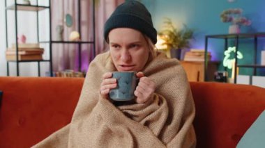 Sıcak battaniyeye sarılı genç bir kadın evde kahve içiyor. Beyaz kadın soğuktan donuyor, kötü hissediyor, sağlıksız. Grip belirtileri gösteren hasta bir kız battaniyeyle kaplanmış evde sıcak çayla ısınıyor..