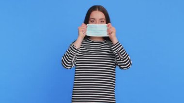 Çizgili bluz giyen, koruyucu tıbbi maske takan, grip virüsü alerjisi koruması olan beyaz bir kadın. Koronavirüs omikron hastalığını önleme konsepti. Hasta kız mavi arka planda izole edilmiş.