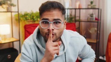 Sessiz olun lütfen. Hintli genç adam işaret parmağını dudaklarına bastırıyor sessizlik işareti yapıyor dedikodu sırrını kimseye söyleme. Evde oturan sakallı Arap adam turuncu sandalyede oturuyor.