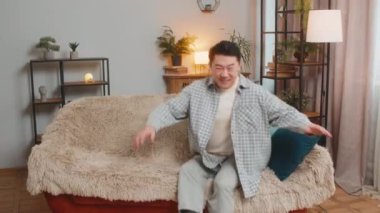 Dertsiz orta yaşlı Çinli adam evinde oturma odasında kafasının arkasında kanepede rahatça oturuyor. Gülümseyen Koreli erkek kanepede dinleniyor. Daire odasına bakıyor..