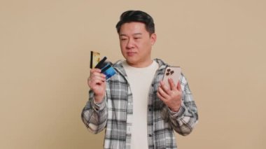 Asyalı, orta yaşlı bir adam kredi kartı kullanıyor, akıllı telefon kullanıyor ve internetten alışveriş yaparken yemek siparişi veriyor. Çinli adam hangi kartın daha karlı olacağını seçer.