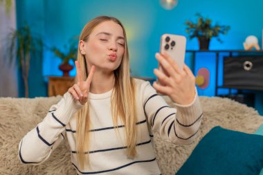 Mutlu Kafkasyalı kadın koltukta oturup selfie kameralı akıllı telefon pozu veriyor. Birden fazla yüz ifadesi sırıtıyor. Dijital, kişisel sosyal paylaşım.