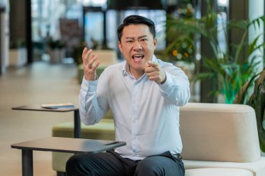 Tişörtlü kızgın yetişkin patron ofisteki modern işyerindeki kameraya bakarak video konuşması yapıyor. Tatminsiz Çinli iş adamı, şirket sorunları hakkında astlarıyla iletişim kuruyor..