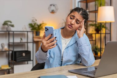 Sinirli Hintli kadın, oturma odasındaki masada otururken akıllı telefon kullanıyor. Başa dokunan üzgün genç kız kaybeder. Ani loto sonuçları ya da kötü haberler karşısında şaşırır. Yaşam biçimi.