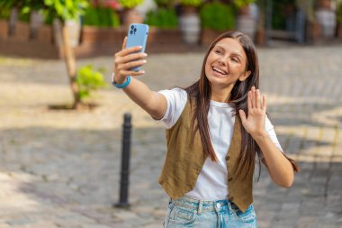 Beyaz kadın blogcu akıllı telefondan selfie çekiyor, abonelerle çevrimiçi video görüşmesi yapıyor, sosyal medya vlog 'u için hikayeler kaydediyor. Şehir caddesinde duran mutlu kız.