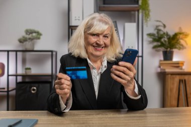 Mutlu Kafkasyalı üst düzey kadın banka kartı ve akıllı telefonu ev ofisinin online alışveriş ödemeleri için kullanıyor. İş anlaşması. Cep telefonu E-bankacılık uygulama servisiyle gülümseyen serbest alımlar.