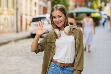 Hoş geldiniz. Kameraya gülümseyen beyaz bir kadın, el sallayarak selam veriyor ya da veda ediyor, dışarıda misafirperver bir yüz ifadesiyle karşılıyor. Şehir sokağındaki mutlu kız. Yaşam tarzları. Yatay