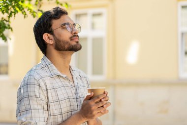 Mutlu Hintli adam sabah kahvesinin tadını çıkarıyor sıcak içecek ve gülümsüyor. Dinleniyorum, ara veriyorum. Şehir merkezindeki caddede dikilen Latin kökenli genç adam kahve içiyor. Dışarıdaki kasaba yaşam tarzları.