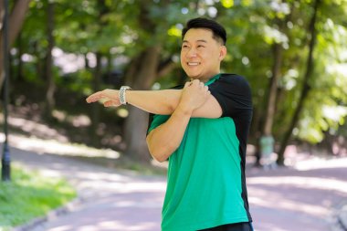 Japon sporcu sporcu, saglikli bir adam, parkta, orman dogasinda, ellerini uzatiyor, kollarini geriyor, sabah sporu, egzersiz, saglik hizmetleri. Sporcu yaşam tarzları.