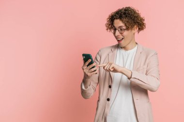 Beyaz adamın mesajlaşması akıllı telefon sosyal medya uygulamalarında içerikli mesajlar paylaşıyor, rahatlama filmleri izliyor. Genç adam cep telefonu gülümsemesi kullanıyor. Pembe arka planda izole edilmiş.