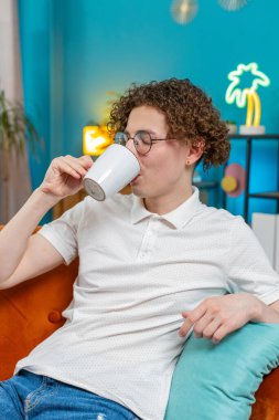 Mutlu genç adam içecek kokusu alıyor sıcak kahve, dinleniyor, dinleniyor. Gülümseyen beyaz adam aroma çayını tek başına içmeyi sever. Oturma odasındaki kanepede oturur..