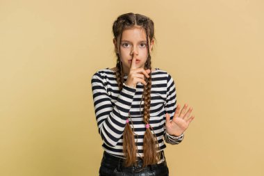 Sessiz olun, lütfen. Küçük çocuk işaret parmağını dudaklarına bastırıyor. Sessiz ol işareti yapıyor. Dedikoduları kimseye söyleme. Çekici çocuklar stüdyo bej arka planda tek başlarına.