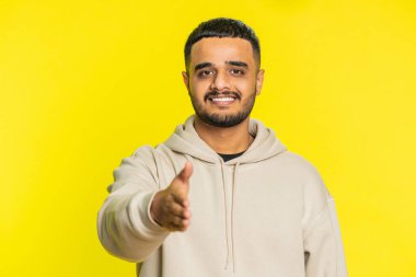 Dost canlısı Hintli Hindu adam kameraya uzandı, el sıkışmayı teklif etti, nazik bir gülümsemeyle, davetle, dayanışma ve güven göstererek selamladı. Sarı arka planda izole edilmiş Arap adam.