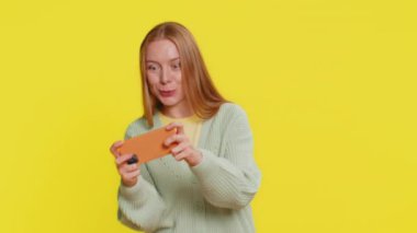 Mutlu, orta yaşlı, heyecanlı beyaz kadın akıllı telefonda yarış arabası simülatörü oyunu oynuyor. Yetişkin kız oyuncu sarı arka planda büyük ikramiyeyi kazandı.