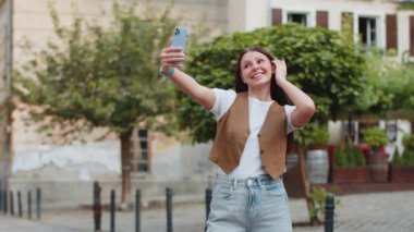 Beyaz kadın blogcu akıllı telefondan selfie çekiyor, abonelerle çevrimiçi video görüşmesi yapıyor, sosyal medya vlog 'u için hikayeler kaydediyor. Şehir caddesinde duran mutlu kız.