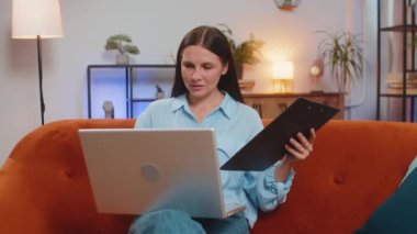 Finans belgeleriyle çalışan serbest çalışan genç bir kadın muhasebeci, çizelgeler için vergileri hesaplıyor ve kanepedeki ev gelirlerinin grafiklerini çıkarıyor. Dizüstü bilgisayarda çalışan, harcama bütçesi planlayan bir kız