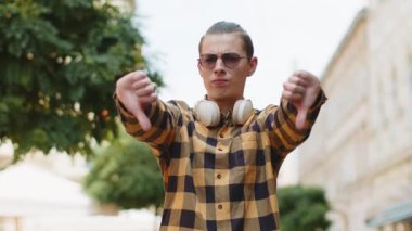 Hoşlanmamak. Üzgün genç bir erkek, işaret dilini gösteriyor, hoşnutsuzluğunu, memnuniyetsizliğini, kötü işini, hatasını ifade ediyor. Şehir caddesinde duran hoşnutsuz stil sahibi turist.