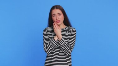 Diş sorunları. Yanağa dokunan genç bir kadın, korkunç bir ifadeyle gözlerini kapatan diş ağrısı, hassas dişler, çürükler. Güzel esmer kız mavi stüdyo arka planında izole edilmiş.