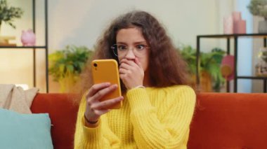 Küçük kız akıllı telefon kullanıyor, oyun oynuyor, beklenmedik piyango sonuçlarını kaybediyor, kötü haber, servet kaybı, başarısız eğitim sınavı. Oturma odasında oturan genç kız kanepede oturuyor.