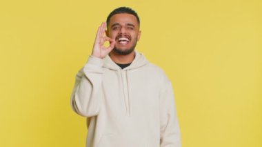 - Tamam. Mutlu Hintli adam onaylayıcı bir şekilde kameraya bakıyor, iyi bir jest yapıyor, olumlu geri bildirim yapıyor, zaferi kutlamak için göz kırpma flörtünü onaylıyor. Sarı arka plandaki Arap adam.