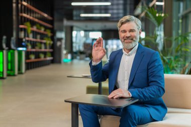 Hoş geldiniz. Kafkas 'lı mutlu iş adamı el sallayarak selam veriyor. Birine hoş geldin diyor. İnternetteki Webinar, uzaktan konuşma. Takım elbiseli girişimci adam modern ofis lobisinde oturuyor..