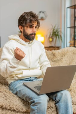 Tartışma. Sinirli genç Hindu serbest çalışan koltukta oturmuş hararetli sohbetlere girişiyor. Üzgün Hintli erkek, apartman odasındaki kanepede dizüstü bilgisayar kullanarak hayal kırıklığı yaşıyor..