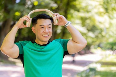 Mutlu genç Japon adam kablosuz modern kulaklık taktı. Koşu koşucusu, spor koşucusu, parkta koşan, müzik dinleyen, müzik dinleyen, koşan, sağlıklı bir yaşam tarzı olan erkek..