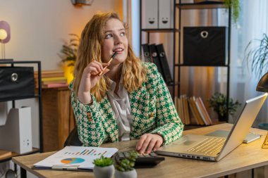 Mutlu gülümseyen genç serbest çalışan evrak işlerini, muhasebe ödemelerini ve ofis masasındaki aylık harcamaları analiz ediyor. Bilgisayarda uzaktan kumandalı çalışan sarışın bir iş kadını.