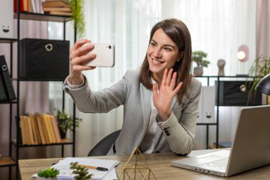 Kafkasyalı genç iş kadını sosyal medyada gülümsüyor pozu vermek için akıllı telefonlardan video çekiyor. Kız serbest çalışma, e-öğrenme, internetten uzak iş.