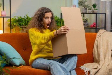 Teslimat paketini açan mutlu beyaz kız çocuğu. Gülümseyen genç çocuk alışverişçisi, çevrimiçi dükkan müşterisi karton kutu açıyor eve hızlı posta gönderimiyle hediye alıyor.