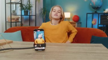 Kafkasyalı genç çocuk evdeki akıllı telefondan son moda selfie videosunu kaydediyor. Dans hareketleri göstermek, masa masa oturmak, sosyal medya için coşkuyla içerik yaratmak.