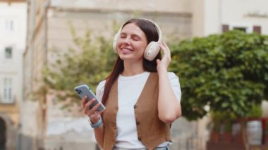 Kablosuz kulaklıklar takmış, açık havada dans eden ve en sevilen disko rock 'n roll müziğini dinleyen mutlu, gevşemiş genç yetişkin kız. Şehir Güneşi Sokağı 'nda beyaz kadın..