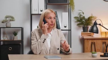 Olgun bir iş kadını cep telefonuyla müşteriye cevap veriyor. Akıllı telefon kullanıyor. Sohbet. Kafkasyalı orta yaşlı kadın uzaktan kumandalı internet işinde çalışıyor, ofis masasında konuşuyor..