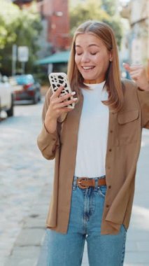 Kafkasyalı genç bir kadın cep telefonuyla kutlama yapıyor iyi haber kazanıyor, kumarhane piyangosunun galibiyetini kazanıyor, açık havada bedava dağıtıyor. Şehir sokağındaki genç kız. Kasaba yaşam tarzları. Dikey.