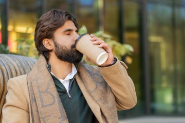 Mutlu Hintli genç adam sabah kahvesinin tadını çıkarıyor sıcak içecek ve dışarıda gülümsüyor. Dinleniyorum, ara veriyorum. Şehir merkezindeki şehir merkezinde oturan ve kahve içen yetişkin bir Arap. Kasaba yaşam tarzları