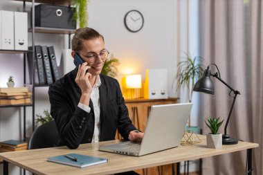 Mutlu Kafkas tarzı genç iş adamı müşteriyle telefon akıllı telefonuyla iletişim kuruyor, ofis masasında dizüstü bilgisayar ağı üzerinde çalışıyor. Takım elbiseli adam internetteki uzak mesafe işini temsil ediyor..