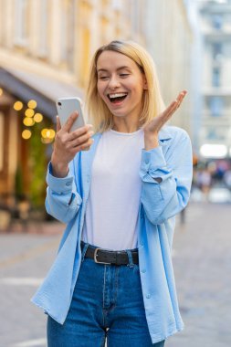 Kafkasyalı genç bir kadın cep telefonuyla kutlama yapıyor iyi haber kazanıyor, piyango büyük ikramiyesi kazanıyor, açık havada dağıtıyor. Şehir caddesinde duran mutlu yetişkin bayan turist. Kasaba yaşam tarzları