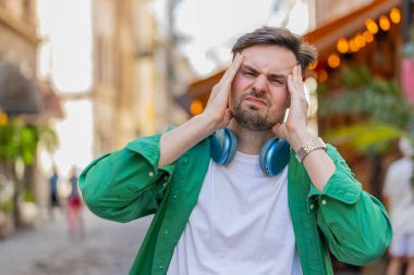 Kafkasyalı adamın baş ağrısı problemini tedavi etmek için tapınakları ovmasından memnun değilim. Genç adam somurtuyor, acı çekiyor yüksek tansiyon şehir caddesinde duruyor..