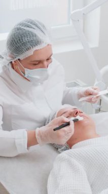 Yüz soyma maskesi, kaplıca güzellik tedavisi, cilt bakımı. Güzellik uzmanları genç kadın yüzüne nemlendirici krem sürüyor. Yüzü sulansın diye. Güzellik salonunda yaşlanma karşıtı kozmetik işlemler yapılıyor. Dikey