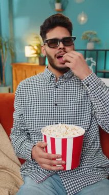 Hintli serbest çalışan, 3 boyutlu gözlük takan, patlamış mısır yiyen ve TV 'de film izleyen bir adam. Gülümseyen İspanyol adam hafta sonları kanepeye oturur ve abur cubur yer. Dikey